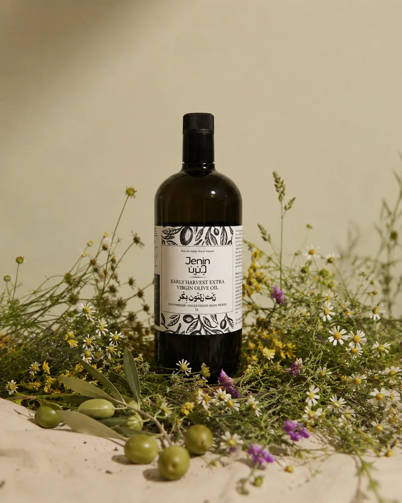 A bottle of Jenin extra virgin olive oil among wildflowers and green olives